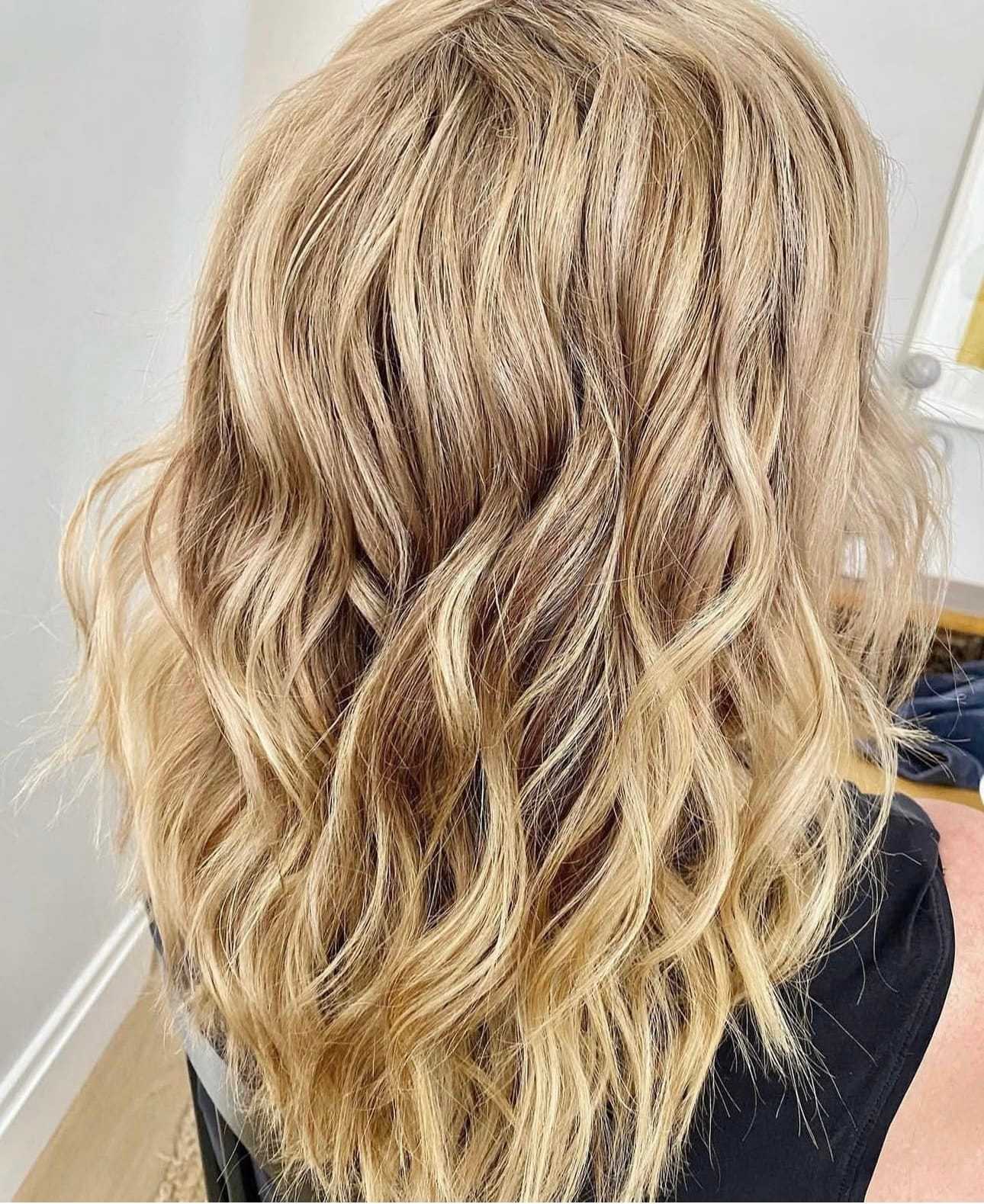 Wavy, shoulder-length blonde hair styled with soft curls.